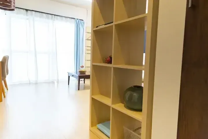 大きな窓から光が差し込むリビングルーム。木製の棚と青いカーテンが特徴的です。