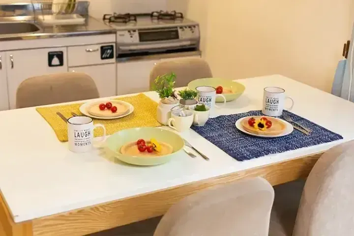 現代廚房中擺放著黃藍餐墊、馬克杯和食物的明亮餐桌。