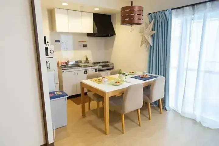 明亮的公寓內設有現代廚房和用餐區，配有木桌、米色椅子和藍色窗簾。
