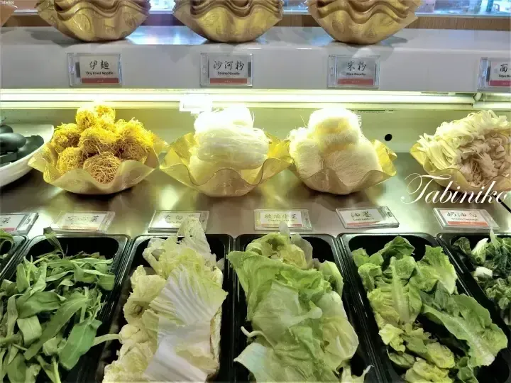 A buffet display featuring various noodles and fresh vegetables in a restaurant setting.