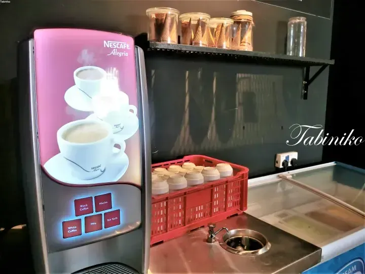 赤いカゴの紙コップとシンクの隣にあるピンク色のネスカフェアレグリアのコーヒーマシン。
