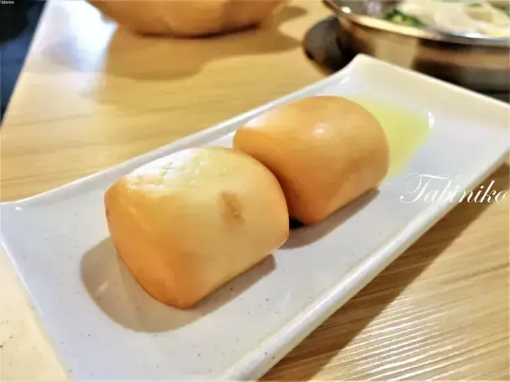 Two golden steamed buns served on a white rectangular plate at a restaurant.