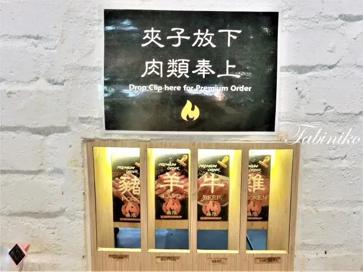 「プレミアムオーダーはここにクリップを」と書かれた看板の下にある、豚・羊・牛・鶏の肉類を分別する木製のクリップ投入口。