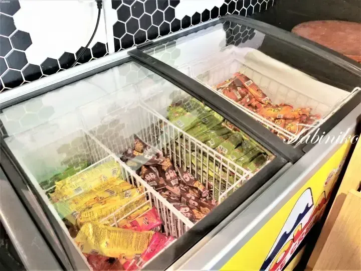 Glass-top chest freezer stocked with colorful ice cream bars and snacks, featuring a yellow side panel with a mountain graphic.