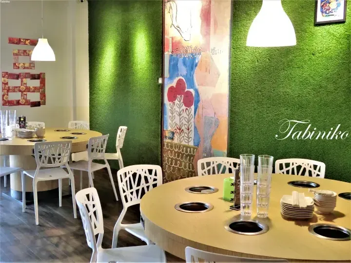 緑の壁と丸テーブルが特徴的なTabinikoの店内。鍋料理用のコンロが設置されたテーブルが並ぶ。