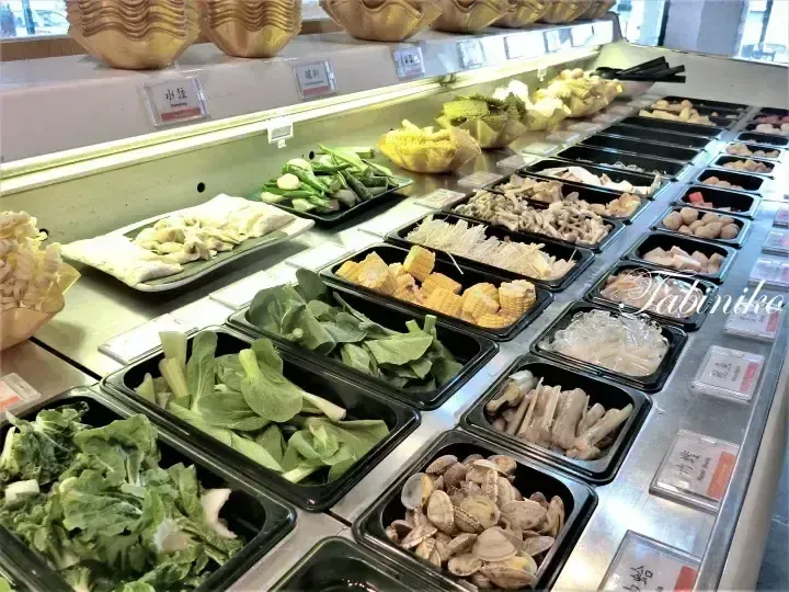 Fresh vegetables, corn, and seafood displayed in black trays at a buffet restaurant.