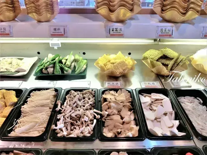 Buffet display of fresh mushrooms, vegetables, and noodles at a Malaysian hotpot restaurant.