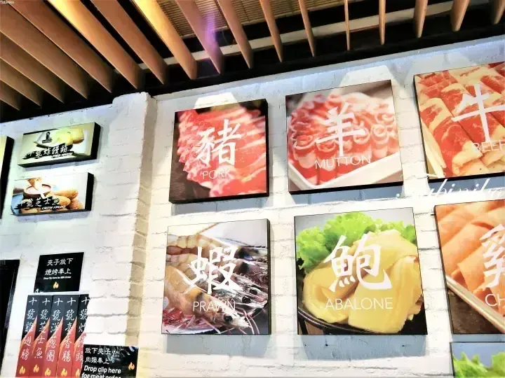 Wall-mounted menu boards displaying images and bilingual text for pork, mutton, beef, prawn, abalone, and chicken at a restaurant.