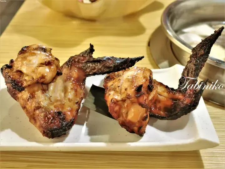 白い長皿に盛られた、焦げ目がついた焼き鳥の翼。