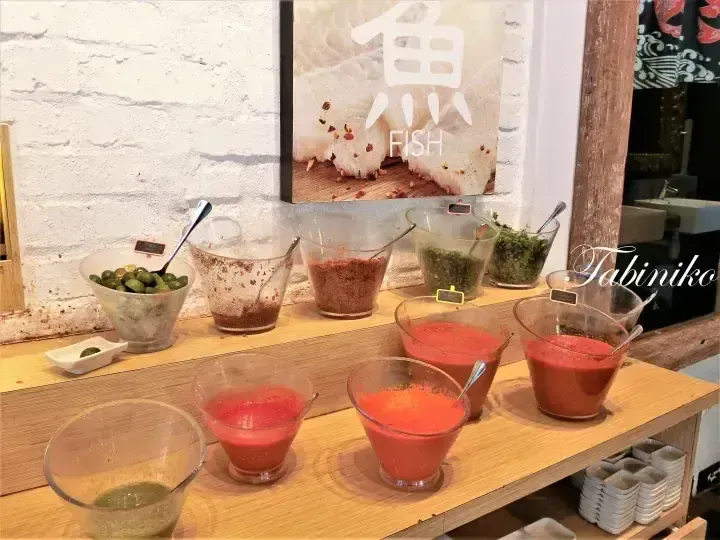 A selection of colorful dipping sauces and condiments displayed in glass bowls on a wooden shelf at a restaurant.
