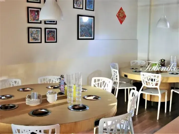 Interior of a hot pot restaurant featuring round wooden tables with built-in burners and white chairs.