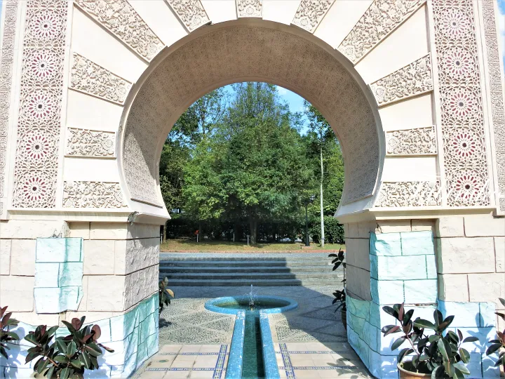 Ornate archway framing a serene garden fountain and lush greenery at a Malaysian property.