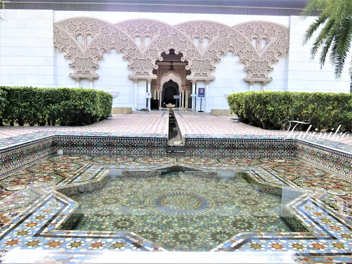 Ornate archway entrance with intricate carvings and a colorful mosaic-tiled pool at Putra Mosque in Putrajaya.