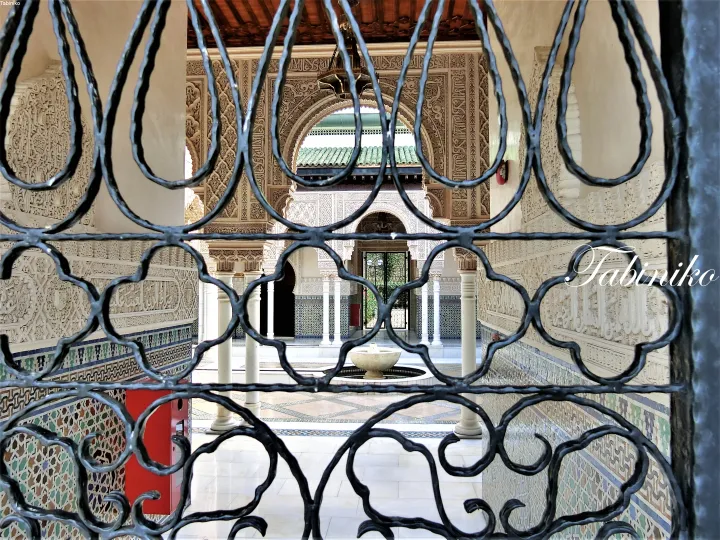 View through ornate ironwork into a courtyard with intricate stucco arches and a central fountain