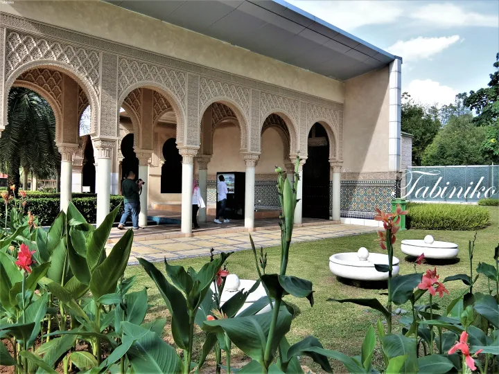 Ornate Moorish arches and tiled walls at a heritage building surrounded by lush greenery and pink flowers.