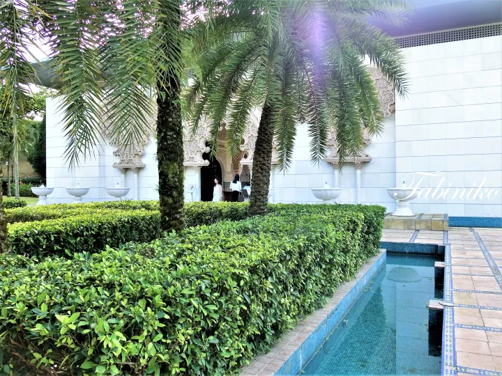 White building with intricate Moorish arches and palm trees beside a blue-tiled pool at a luxury resort in Malaysia.