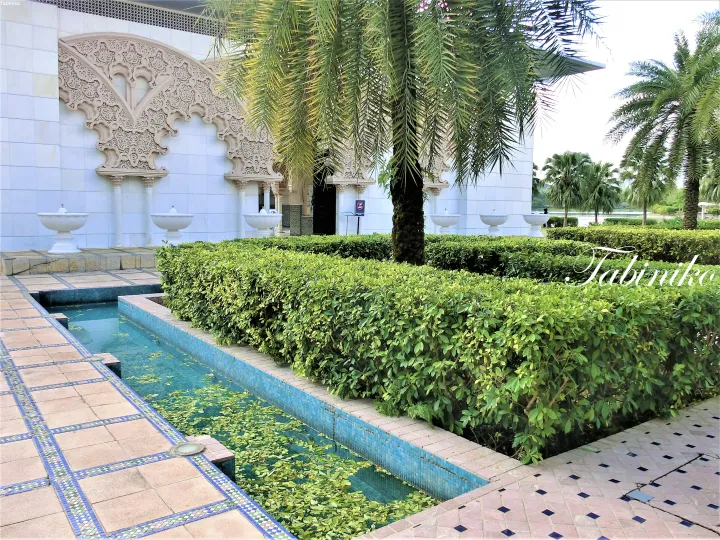 Ornate arches and fountains adorn the white facade of the Putrajaya Mosque, surrounded by manicured hedges and palm trees.