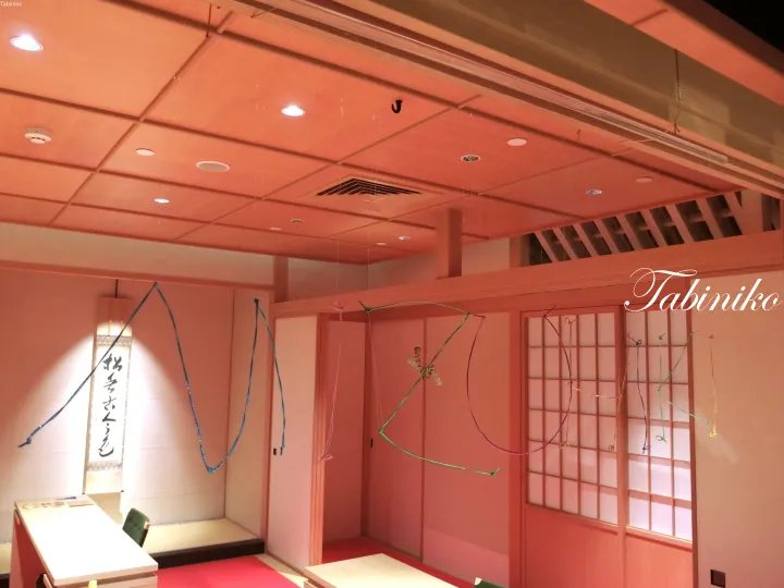 Interior of a traditional Japanese room with tatami mats, shoji screens, and hanging blue decorations.