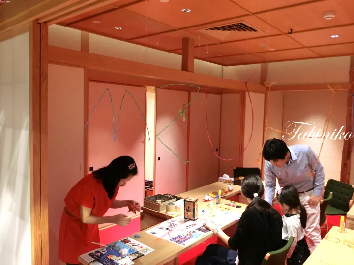Family enjoying a hands-on craft activity at a warm-toned wooden workshop table in a cozy indoor setting.
