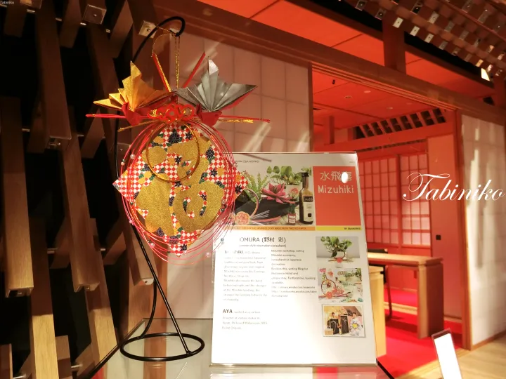 Traditional Japanese decorative ornament displayed beside an informational sign for Mizuhiki and Omura at a cultural exhibition.