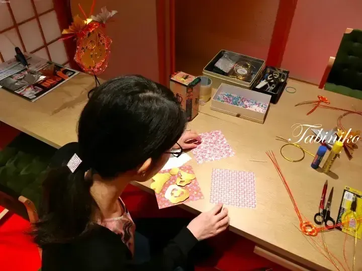 一名女子在桌前製作摺紙，背景有裝飾燈籠。