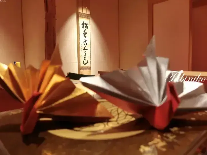 背景有書法掛軸的桌上金色和銀色摺紙鶴。
