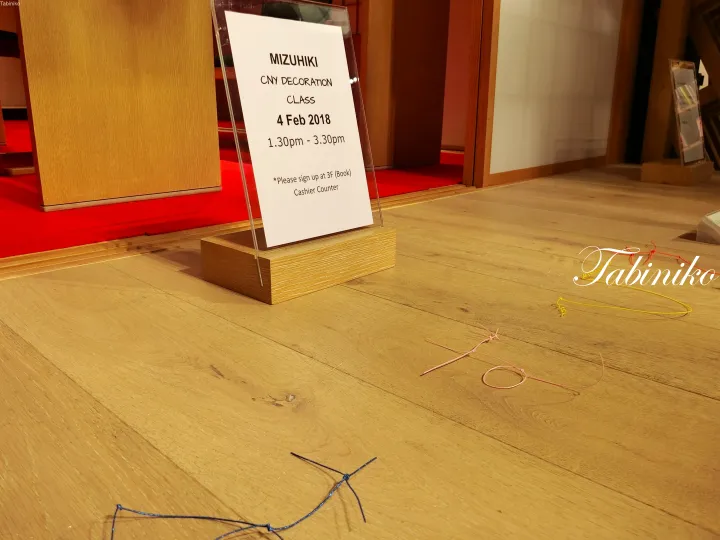Sign for MIZUHIKI CNY decoration class at Tabiniko on 4 Feb 2018 with colorful string decorations on the wooden floor.