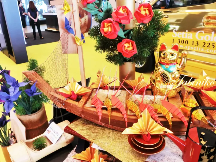 A festive display featuring a wooden boat with origami decorations, a golden lucky cat, and red roses at a Setia property event.