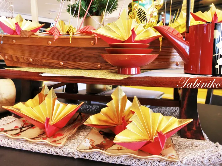 Traditional Japanese New Year display featuring origami boats, red lacquerware, and a wooden boat centerpiece.