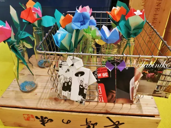 木箱の上に置かれたガラス瓶に入った折り紙の花と、ワイヤーバスケットに入ったグリーティングカード。