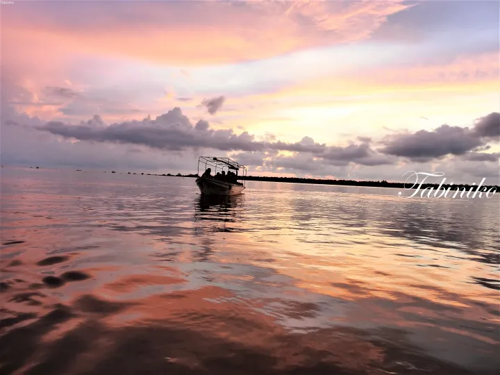 Boat with passengers glides across calm waters under a vibrant pink and purple sunset sky.