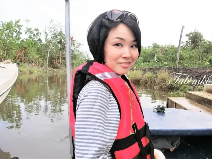身穿条纹衫和红色救生衣的女子，在绿树环绕的河流上乘船游览。