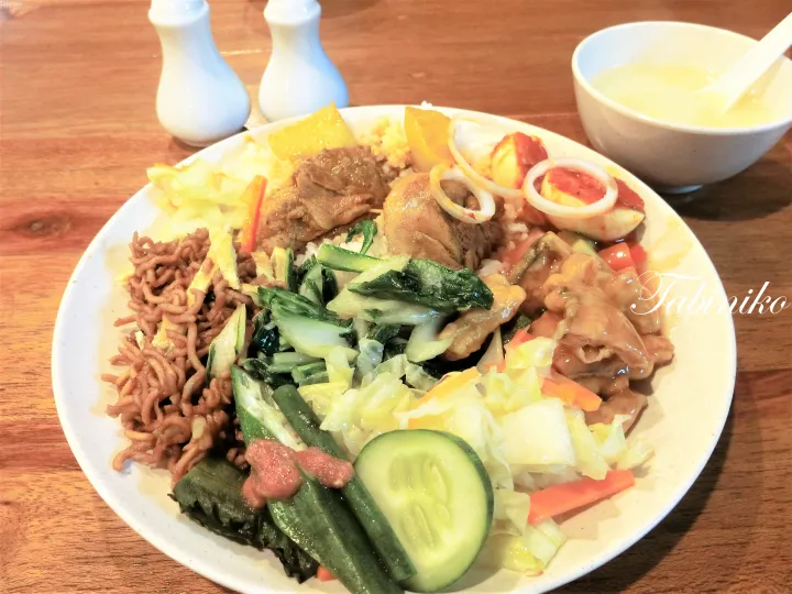A plate of Malaysian rice with assorted dishes including noodles, vegetables, meat, and egg, served with soup.