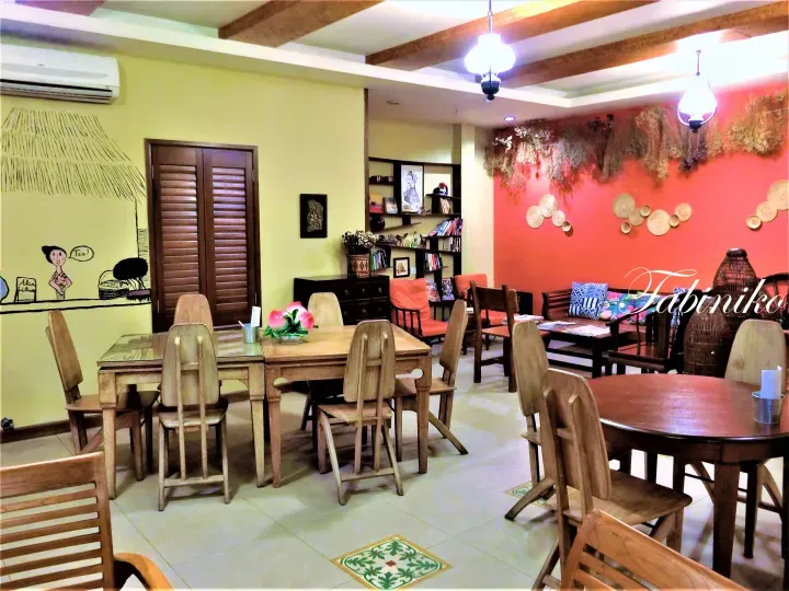 Warm interior of Tabiniko cafe featuring wooden furniture, a mural, and a coral wall with dried floral decor.