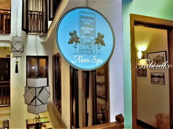 酒店走廊内悬挂着写有“Alam Spa”字样及建筑插图的蓝色圆形招牌，旁边装饰有几何造型的吊灯。