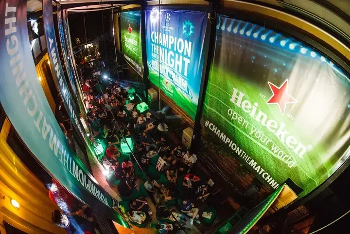 Crowd watching football at Heineken Champion Night event with large banners.