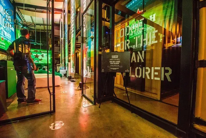 A person enters the Heineken Champion Hostel, a container hotel in Malaysia with vibrant green lighting and promotional signage.