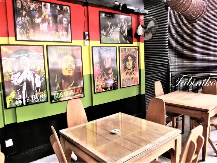 Interior of a Jamaican-themed restaurant featuring wooden tables and walls decorated with Bob Marley posters in red, yellow, and green.