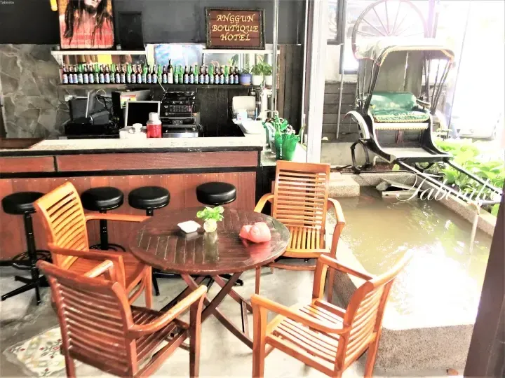 Anggun Boutique Hotel bar area with wooden furniture, a water feature, and a decorative rickshaw.