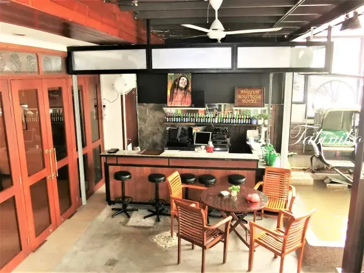 Bar area at Anggun Boutique Hotel featuring wooden furniture, a Bob Marley poster, and a view of a traditional trishaw.