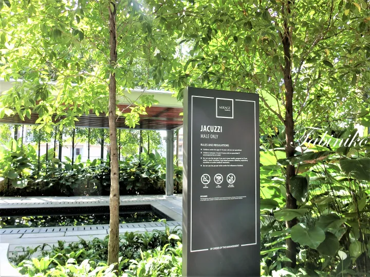 Black signage at Mirage Residence indicating a male-only jacuzzi with rules and regulations surrounded by lush greenery.