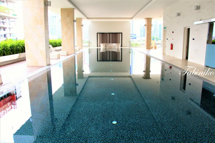 Modern infinity pool with dark mosaic tiles at a Kuala Lumpur high-rise, featuring beige pillars and city skyline views.