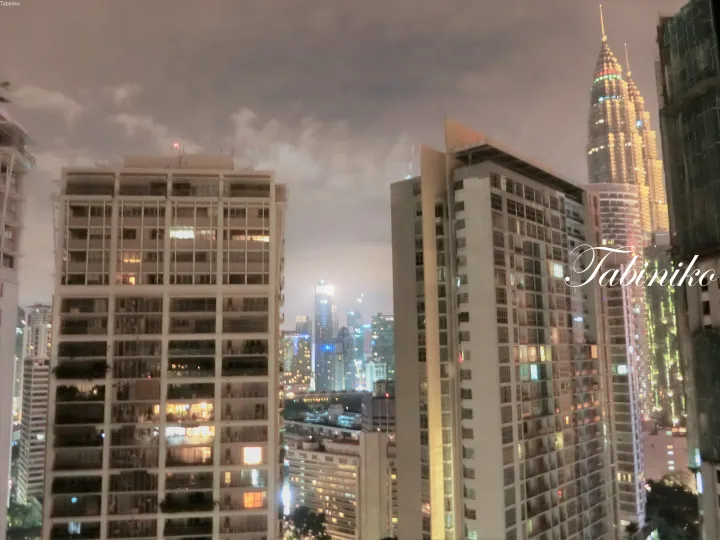 Night view of Kuala Lumpur skyline featuring the Petronas Twin Towers and surrounding high-rise residential buildings.