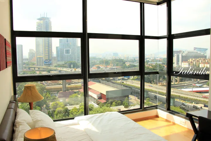 Bright hotel room with a large window overlooking a cityscape, highway, and modern buildings.