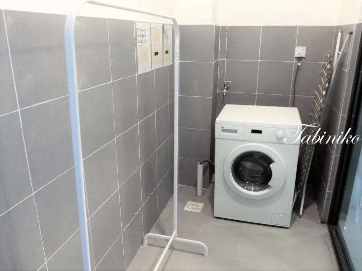 White washing machine in a tiled laundry room with a drying rack and ironing board.
