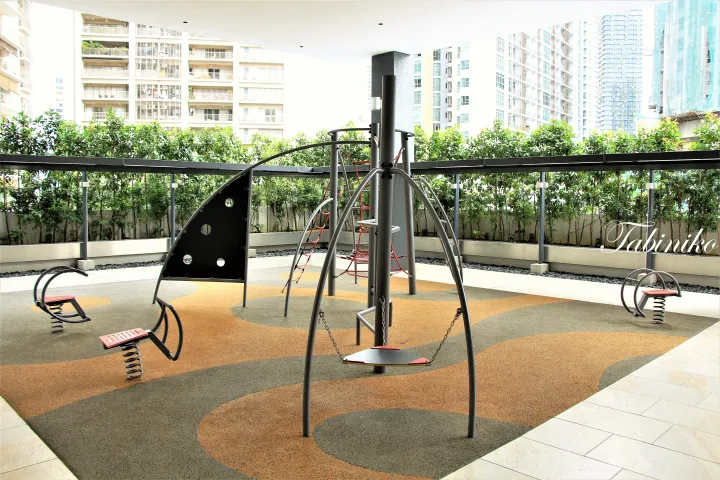 Modern playground with spring riders and a swing set on colorful rubber flooring at a high-rise residential complex.
