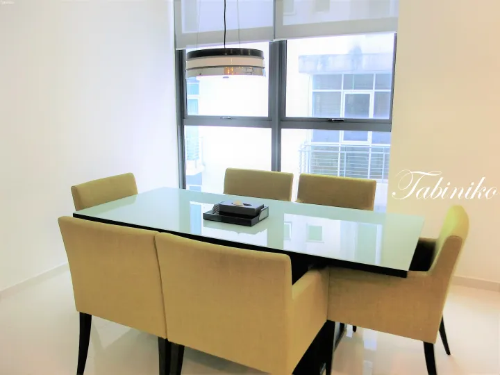 Modern dining table with beige upholstered chairs and a glass top in a bright room with large windows.