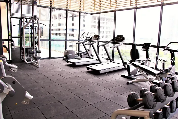 透过大窗户可俯瞰城市建筑的现代化健身房，配有Technogym跑步机和哑铃