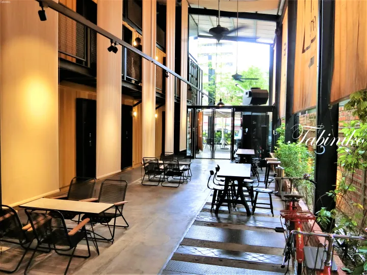 Modern industrial-style corridor with wooden walls, black metal tables, and bicycles parked near a glass entrance.