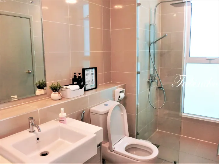 ベージュタイルのモダンなバスルーム。ガラス張りのシャワー、白い洗面台、トイレを備えたマレーシアの物件。